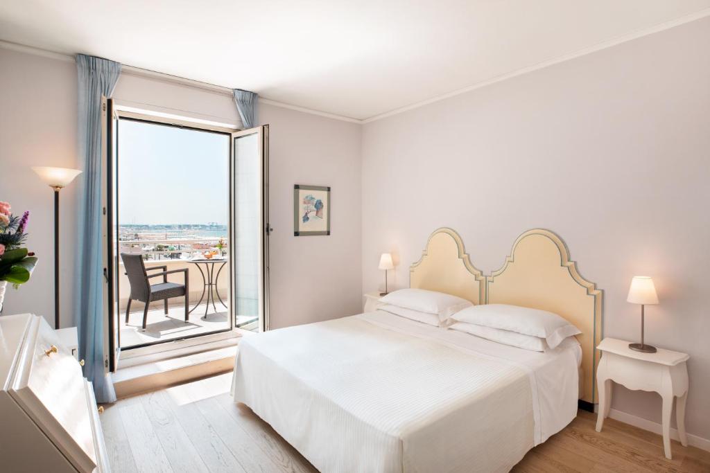 a white bedroom with a bed and a balcony at Hotel Sina Astor in Viareggio