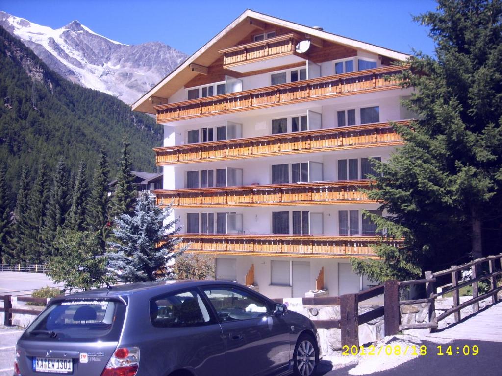 une voiture garée devant un grand bâtiment dans l'établissement Haus Apollo, à Saas-Almagell