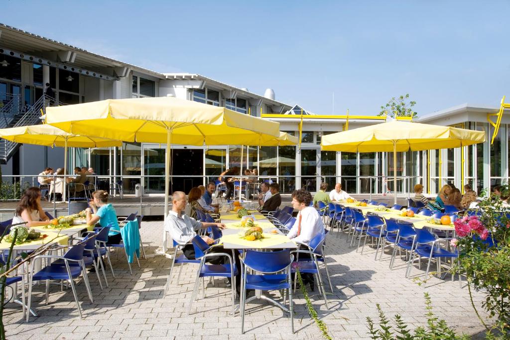 eine Gruppe von Menschen sitzt an Tischen mit gelben Sonnenschirmen in der Unterkunft GenoHotel Karlsruhe in Karlsruhe