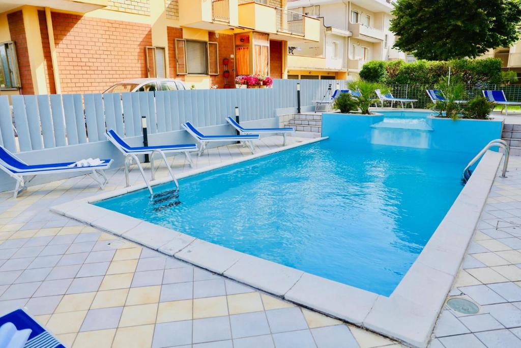 a swimming pool with blue chairs and a fence at Hotel A Casa Nostra in Rimini