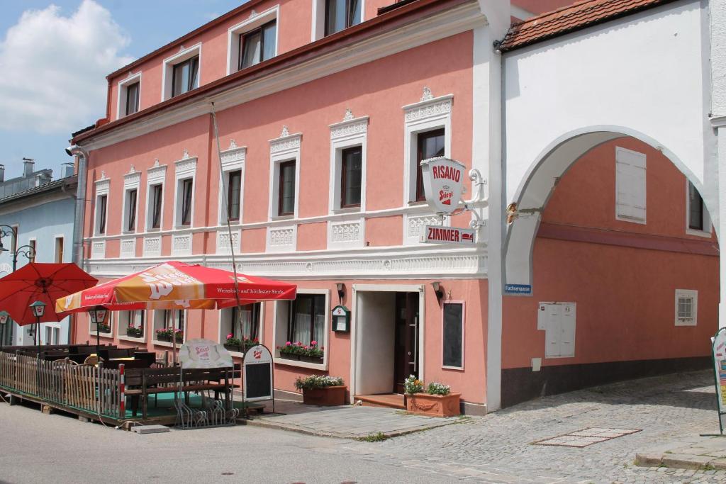 różowy budynek ze stołem i parasolem przed nim w obiekcie Gasthof-Cafe-Risano w mieście Haslach an der Mühl