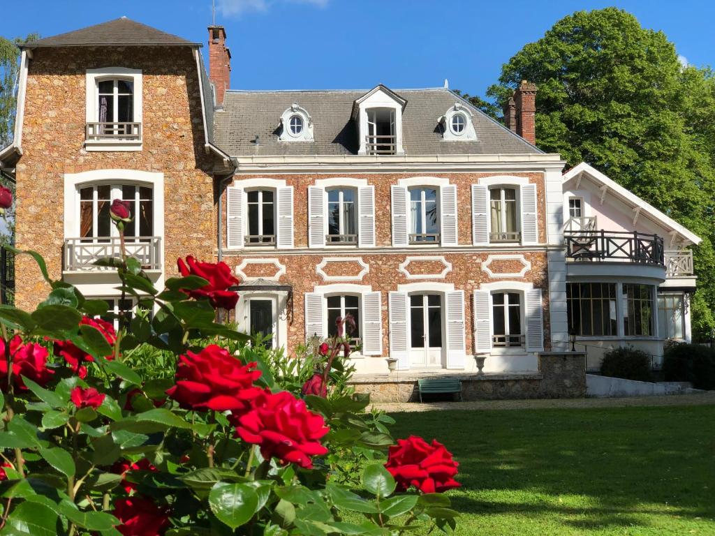 une grande maison en briques avec des fleurs rouges devant elle dans l'établissement La villa rochette, à Forges-les-Bains