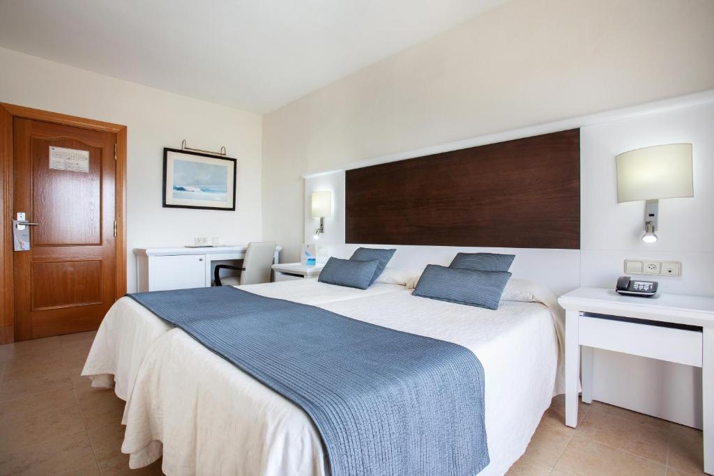 a bedroom with a large white bed with two blue pillows at Grupotel Amapola in Playa de Muro