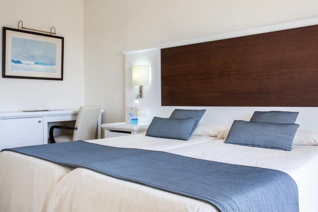 a bedroom with a large bed with two blue pillows at Grupotel Amapola in Playa de Muro
