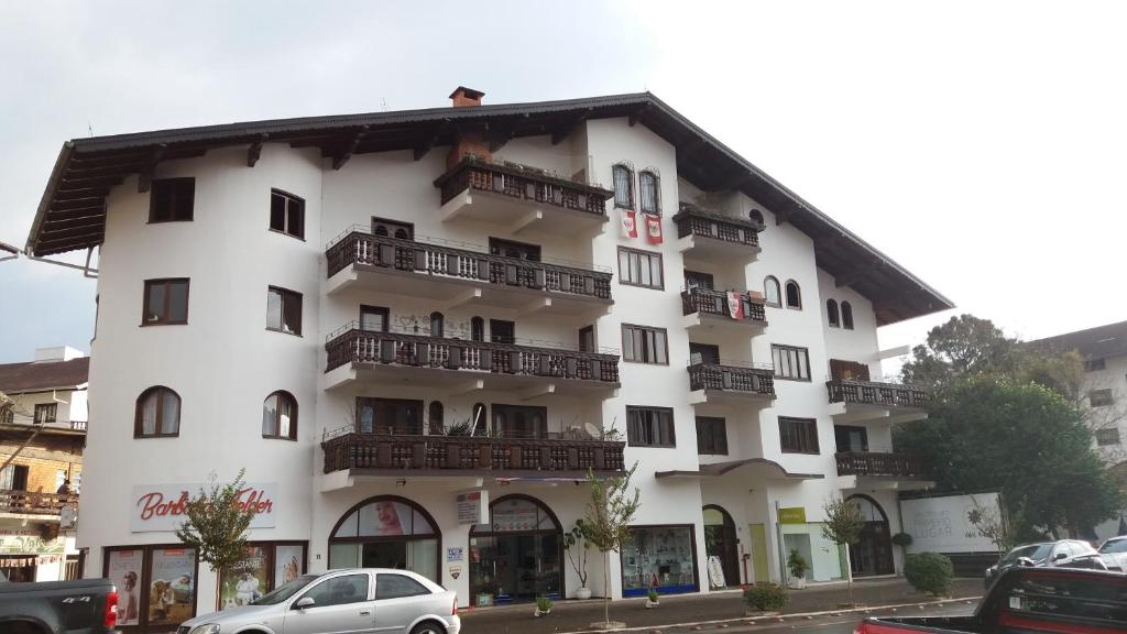 a white building with balconies and cars parked in front of it at Hospedagem da Escultora in Treze Tílias