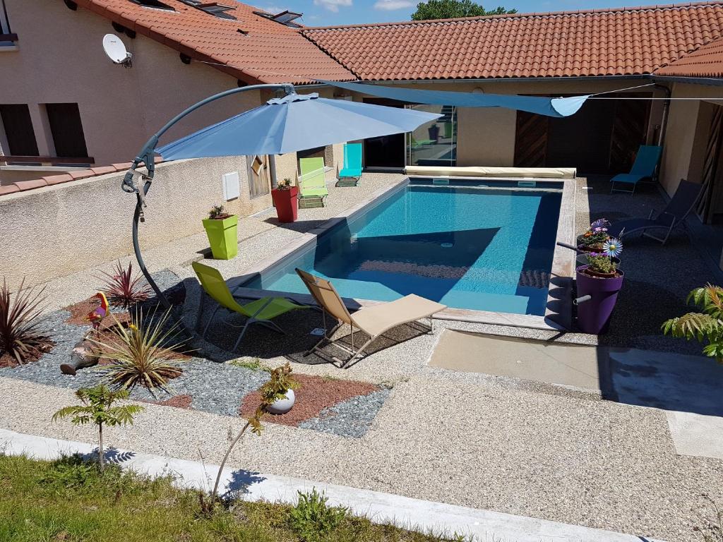 a swimming pool with an umbrella and chairs next to a house at Hôtel Les Rives D'Allier in Reilhac