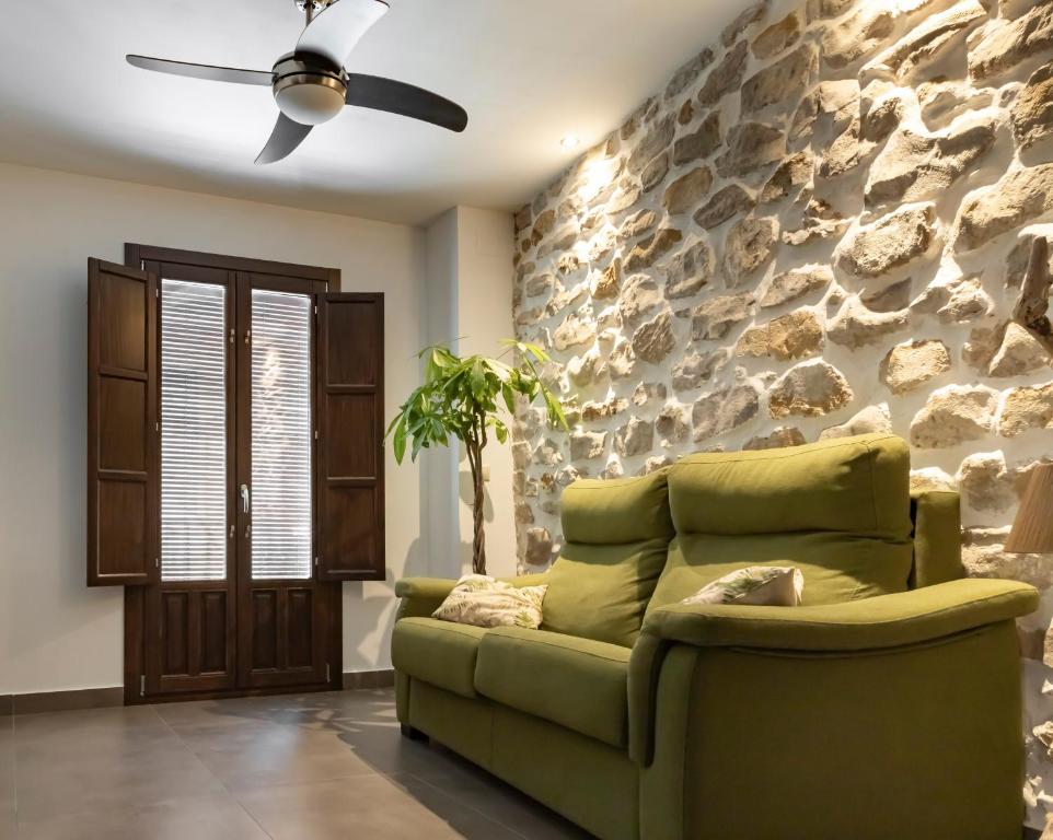 a living room with a green couch and a stone wall at Alojamiento San Nicolas in Úbeda