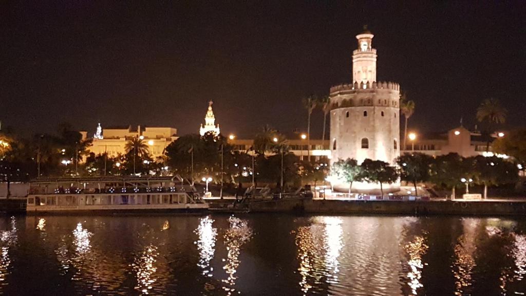 un edificio con una torre de reloj junto a un río por la noche en La Corrala de Triana, en Sevilla
