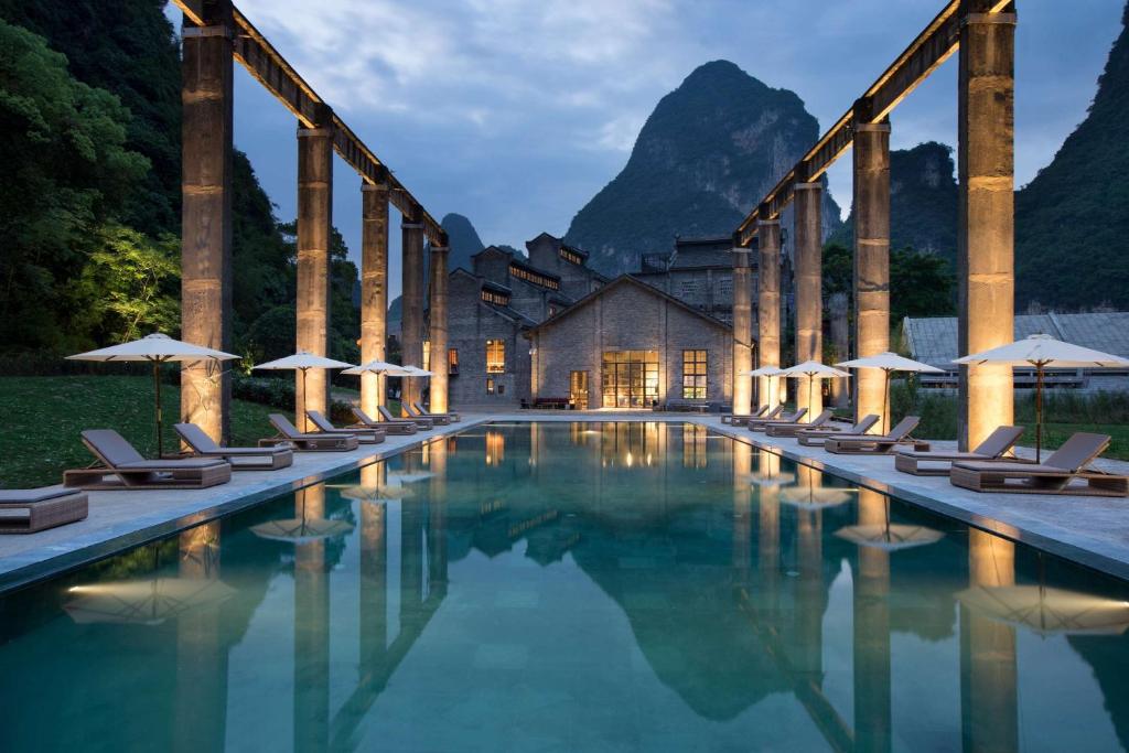 a hotel with a pool with chairs and umbrellas at Yangshuo Sugar House in Yangshuo