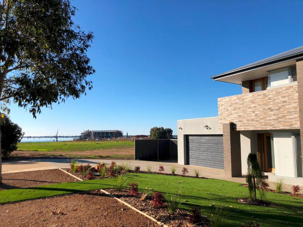 a house with a grass yard next to a building at Lake Resort on Black Bull in Yarrawonga