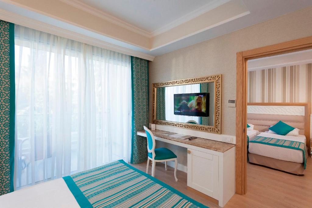 a bedroom with a bed and a desk with a television at Karmir Resort & Spa in Kemer