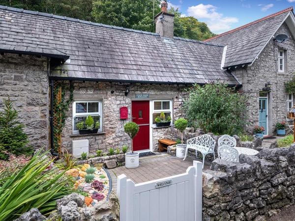 a stone house with a red door and a white fence at Coachhousebungalow in Grange Over Sands