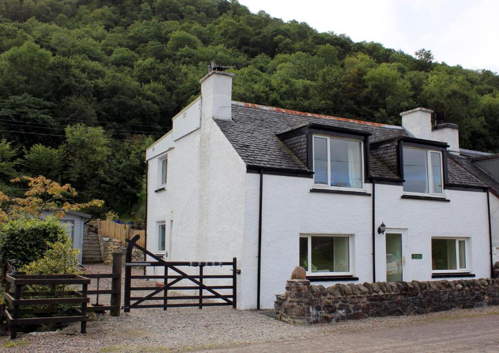 una casa bianca con una recinzione di fronte a una montagna di Arivonie Lochside Cottage a Glencoe