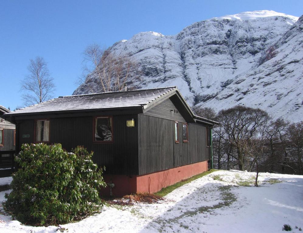 uma casa preta com uma montanha coberta de neve ao fundo em Beech Chalet em Glencoe