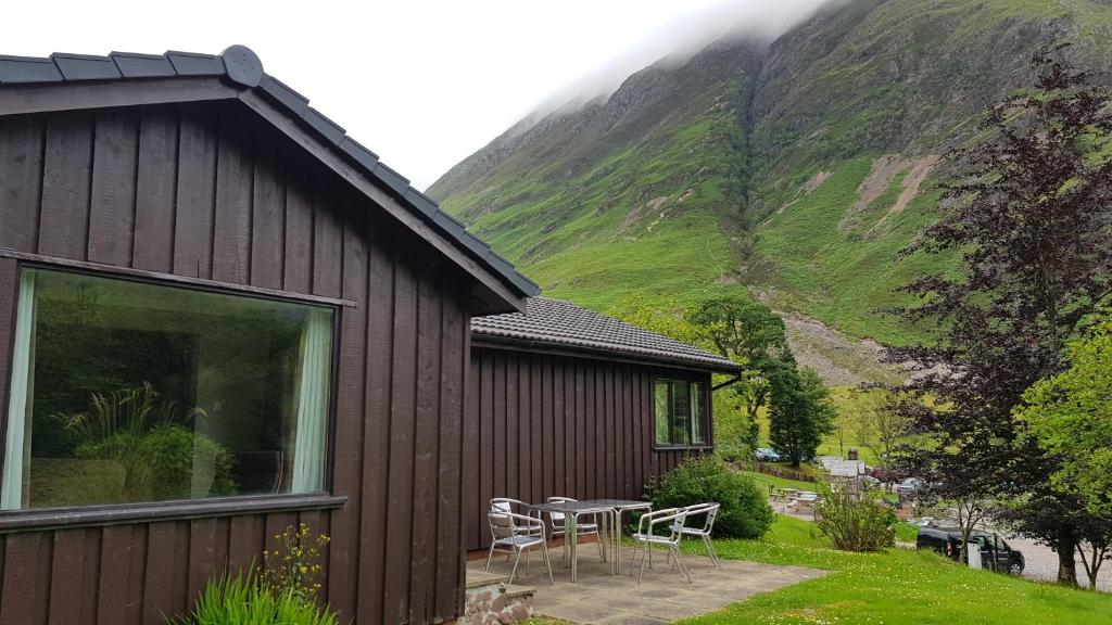 a house with a table and chairs in front of a mountain at Oak Tree Lodge in Ballachulish