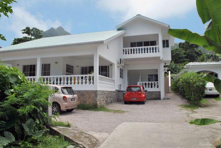 a white house with cars parked in front of it at Rowsvilla Guest House in Beau Vallon