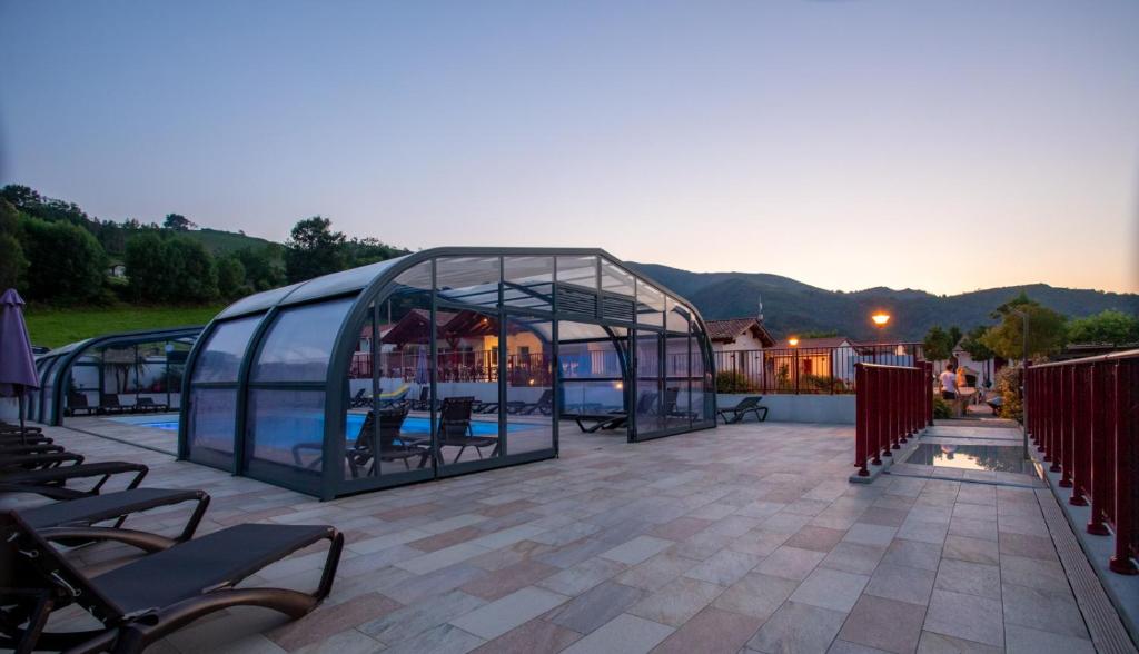 a glass greenhouse on a patio with mountains in the background at Domaine Chalets Larlapean in Saint-Martin-dʼArrossa