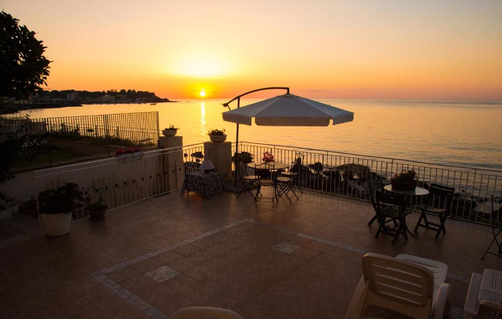 einen Sonnenuntergang auf einem Balkon mit Tischen und einem Sonnenschirm in der Unterkunft Appartamento in Villa Agnese in Acitrezza