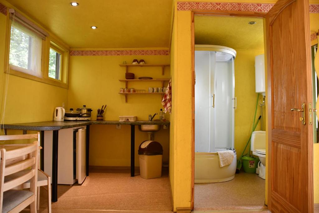 a yellow kitchen with a sink and a tub at Kempings Ezerpriedes in Burtnieki