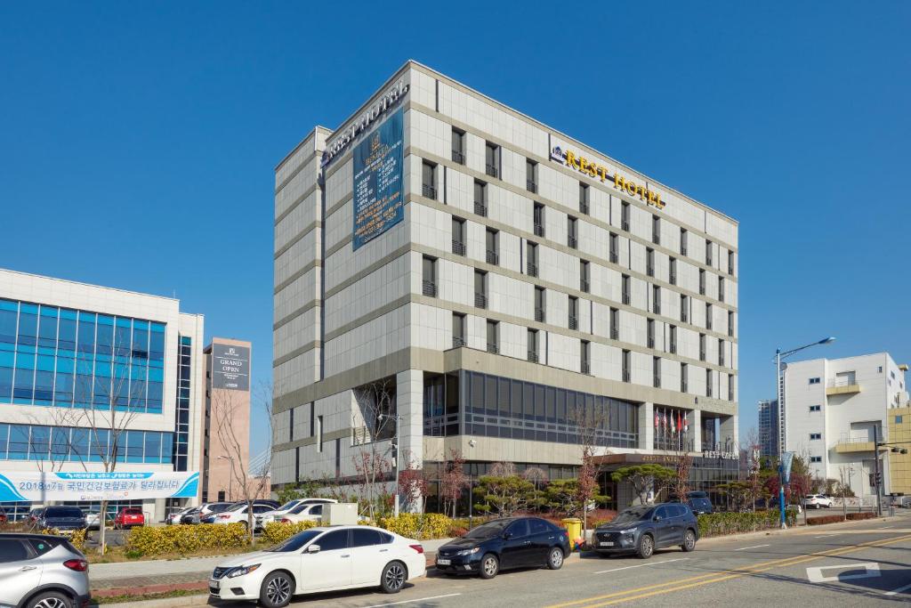 Un grand bâtiment avec des voitures garées devant lui dans l'établissement Rest Hotel, à Gimpo