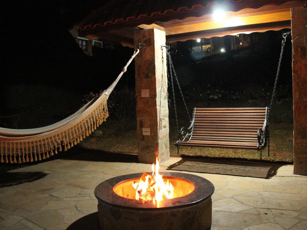 a fire pit with a hammock and a bench at night at Pousada Winterhaus in Monte Verde