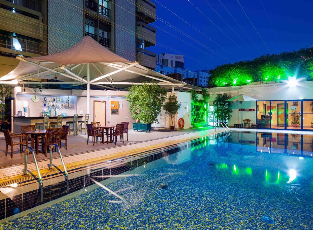 uma piscina com uma mesa e cadeiras e um guarda-sol em Novel Hotel City Center em Abu Dhabi