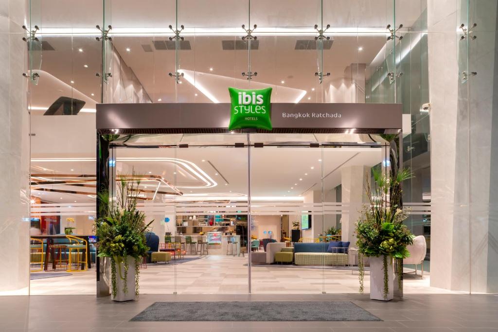 A glass-fronted lobby entrance with greenery, lounge seating, and bright geometric lighting.
