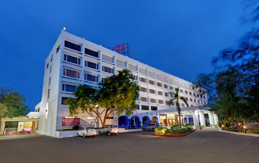 un edificio bianco con un parcheggio di fronte di SRM Hotel Trichy a Tiruchchirāppalli