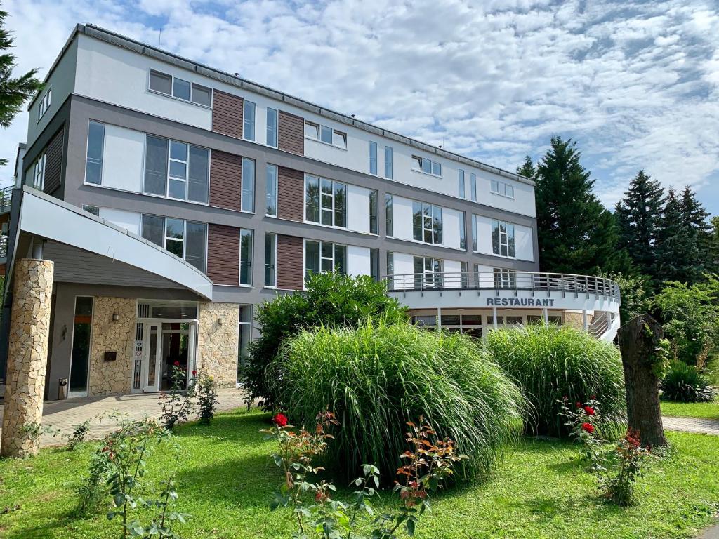 een groot gebouw met een tuin ervoor bij Well Hotel in Harkány