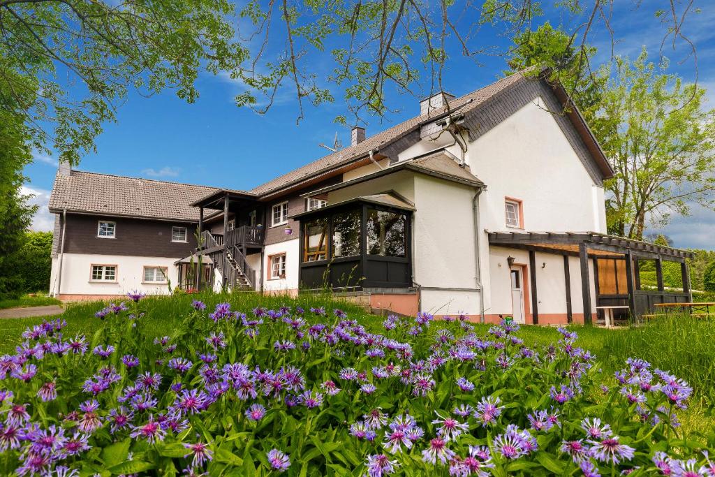 uma casa com flores roxas em frente em Landhaus Schnorrenberg, Wellness & Nature em Hellenthal