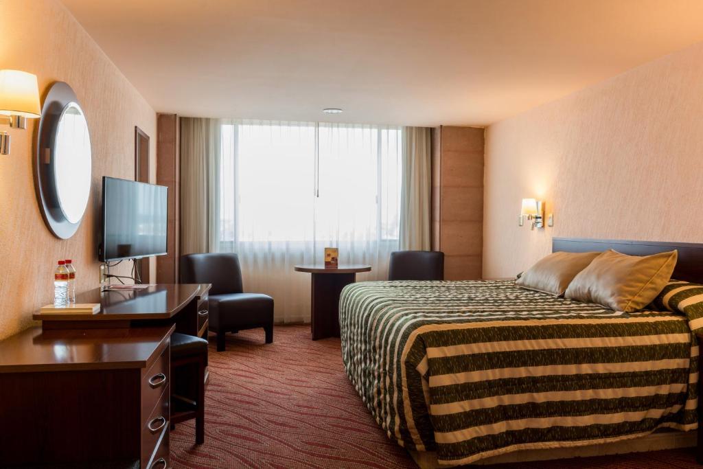 アグアスカリエンテスにあるHotel Real Plaza Aguascalientesのベッド、デスク、テレビが備わるホテルルームです。