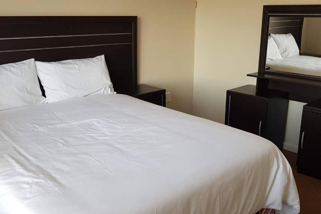 a bedroom with a large white bed and a mirror at Neat Haven Self Catering in Grahamstown