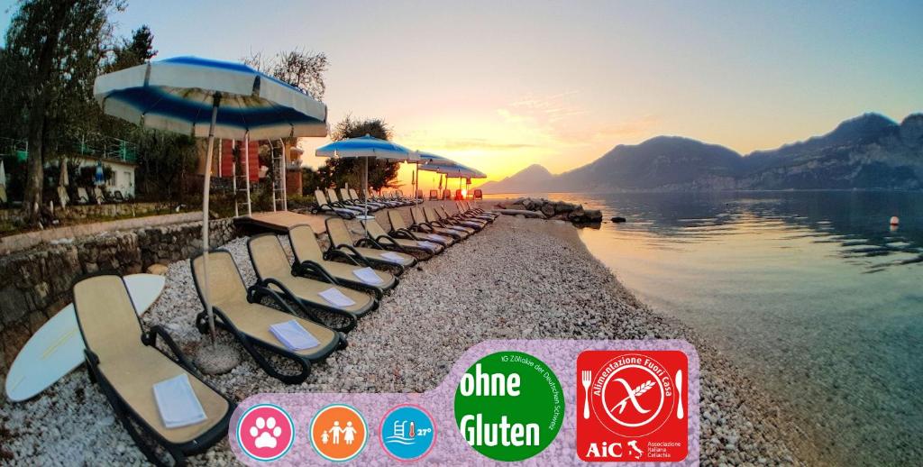 a row of chaise lounges and umbrellas next to a lake at Hotel Eden in Brenzone sul Garda