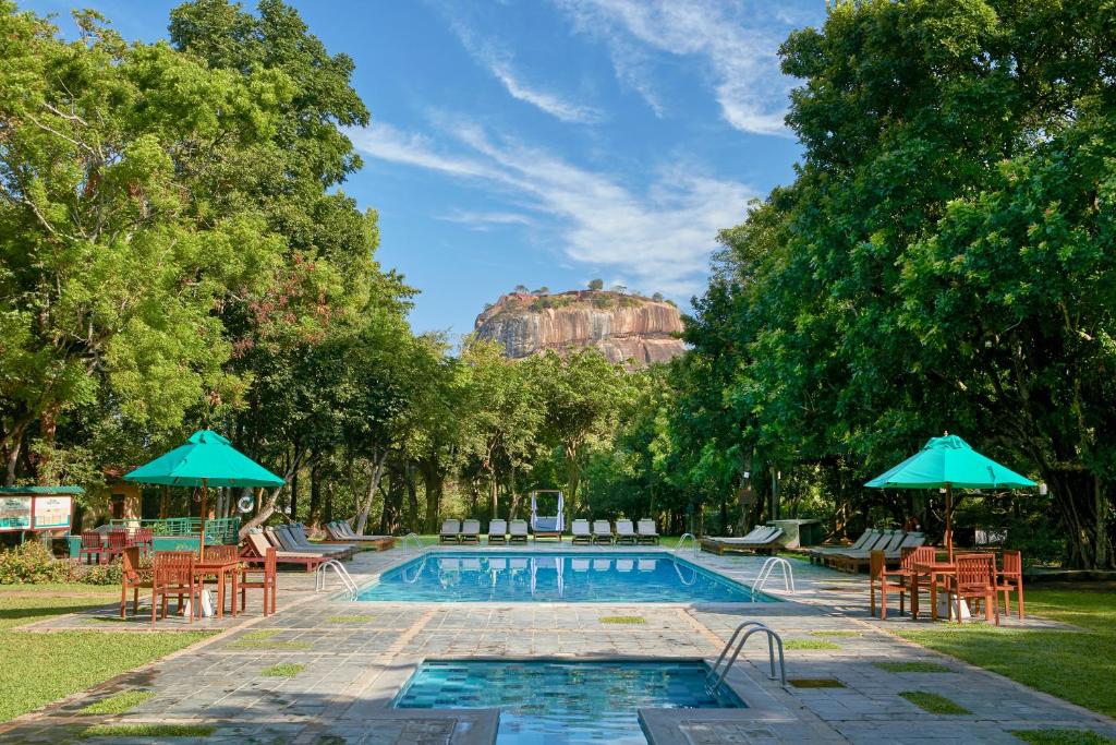 a swimming pool with chairs and umbrellas next to at Hotel Sigiriya in Sigiriya