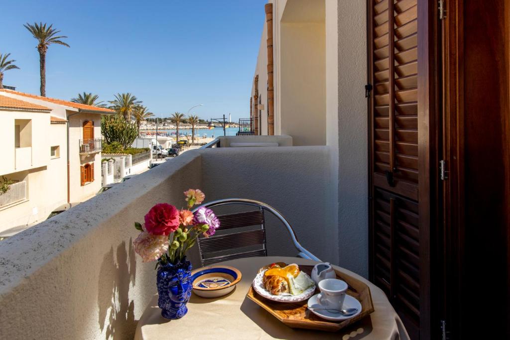 une table avec une assiette de nourriture et de fleurs sur un balcon dans l'établissement Hotel Riva Del Sole, à San Vito Lo Capo
