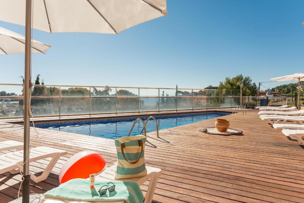 einen Pool mit Stühlen und einem Sonnenschirm auf einer Holzterrasse in der Unterkunft Pierre & Vacances Villa Romana in Tossa de Mar