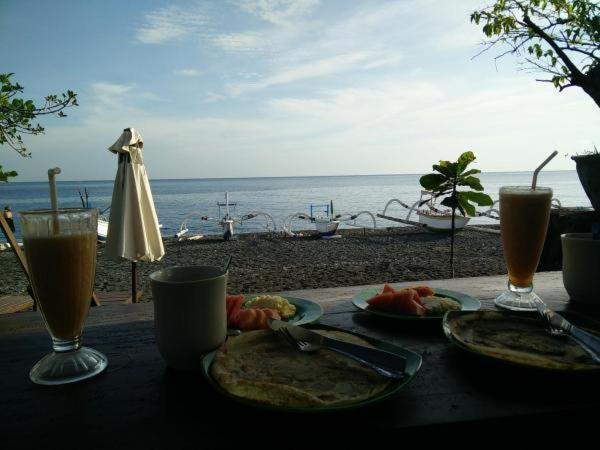 een tafel met borden eten en drinken op het strand bij Putra'Lebah Amed Guest House in Amed
