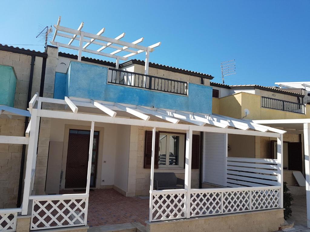 una casa con una veranda bianca e un edificio blu di Casa La Rosa - Residence Rada delle Tortore a Marzamemi