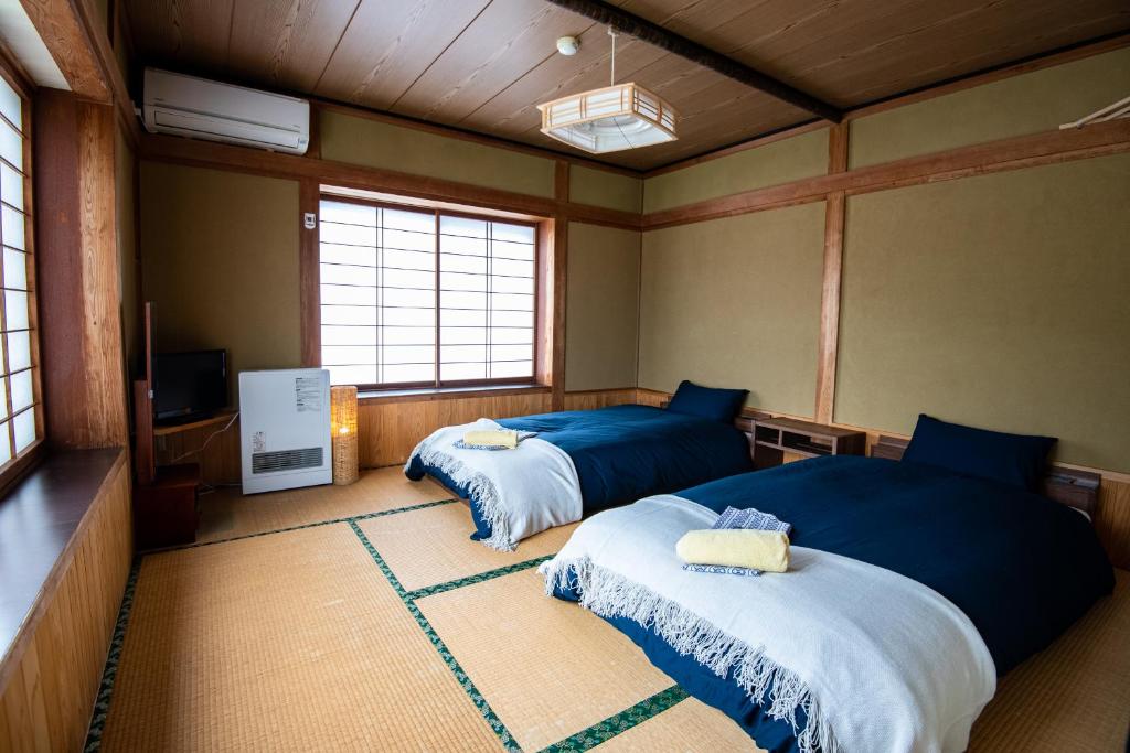 a room with two beds and a tv and windows at Toemu Nozawa Lodge in Nozawa Onsen