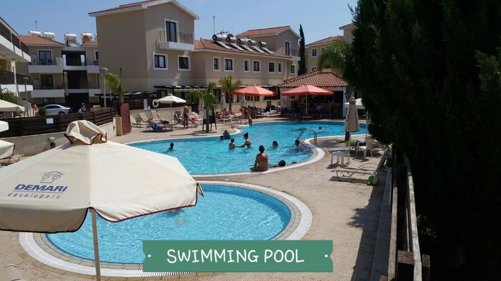 una piscina con sombrilla y gente en ella en CHRIS'S KYKLADES HOLIDAY APARTMENT, en Paralimni