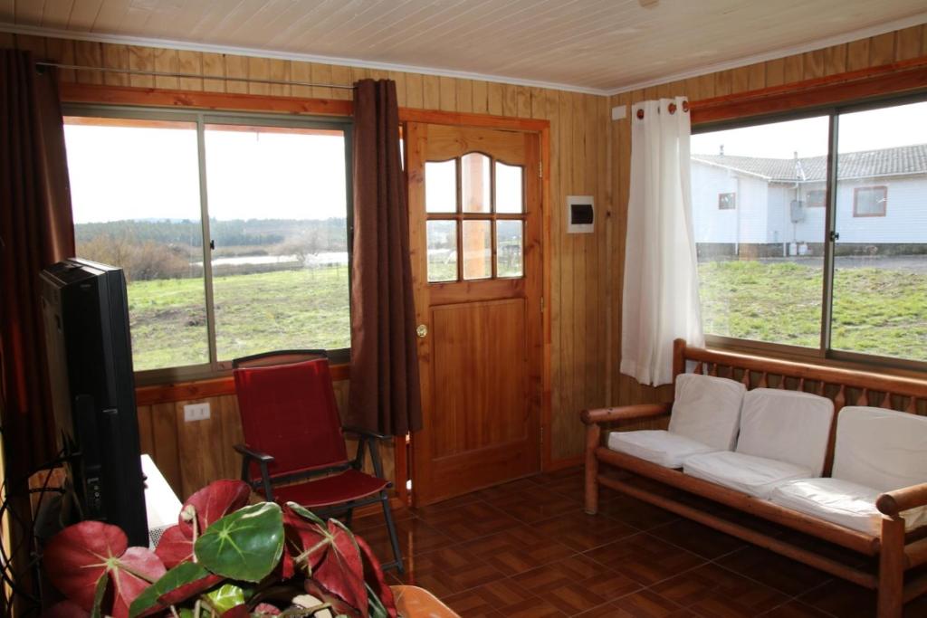 a living room with a couch and a tv and windows at Laguna Verde Cabaña in Nueva Imperial