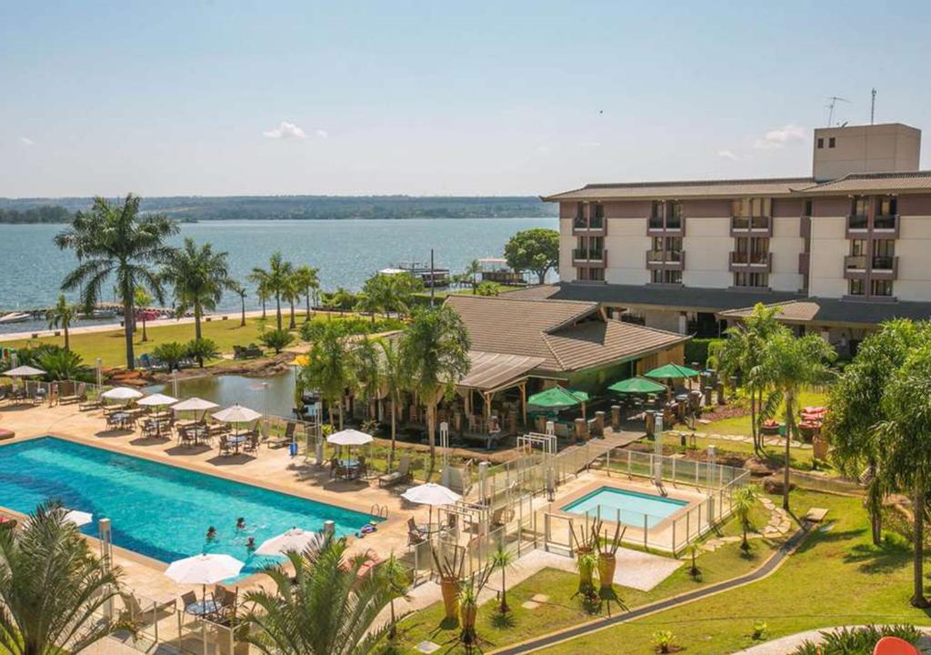 a beach area with a pool, lawn chairs, and a large building at Life Resort Hplus Long Stay in Brasília