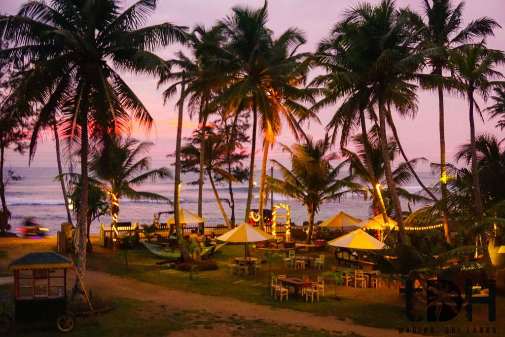 een strand met tafels, parasols en palmbomen bij The Doctor's House in Matara