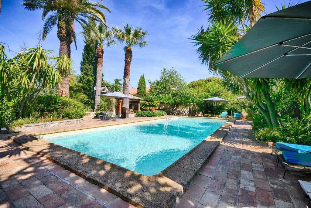 a swimming pool with palm trees and a blue umbrella at Les Bastidieres - Cap Brun in Toulon