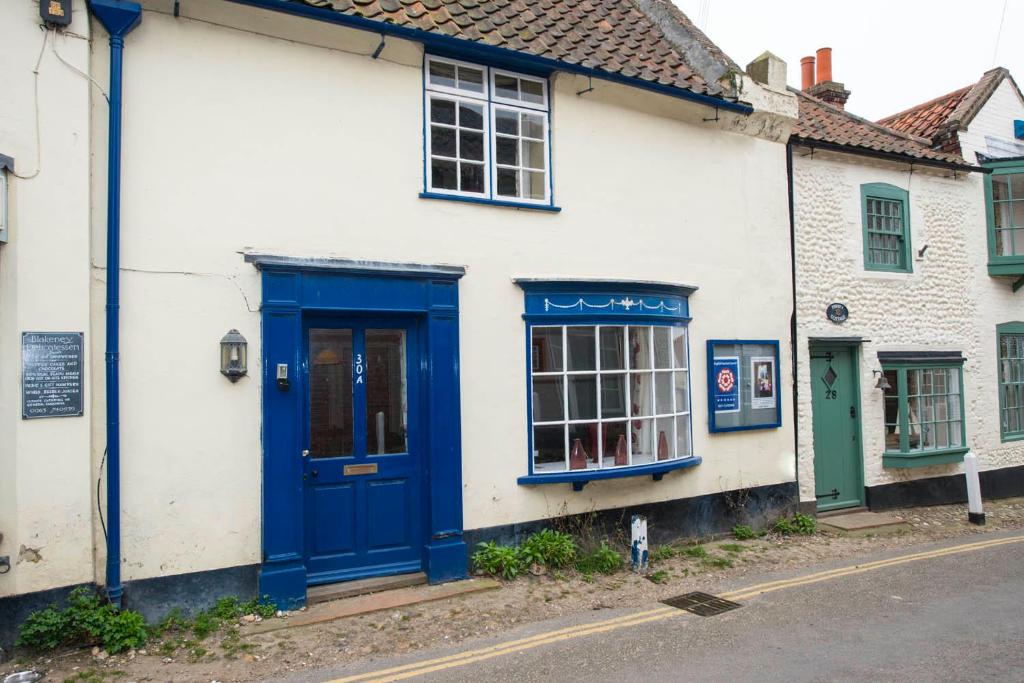 a white building with a blue door and windows at The Bittern in Blakeney