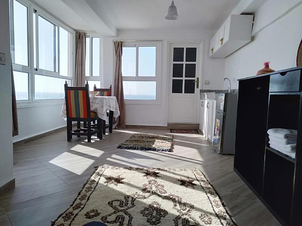 a living room with a table and a kitchen with windows at Appartements la grotte in Essaouira
