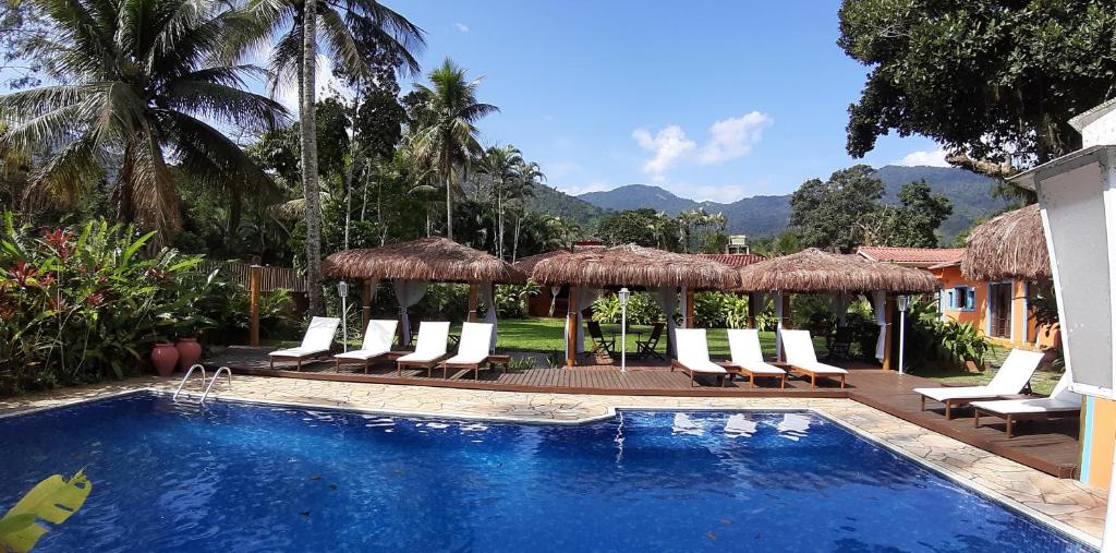 a pool with chairs and umbrellas next to a resort at Pousada Canoa Caiçara Ilhabela in Ilhabela