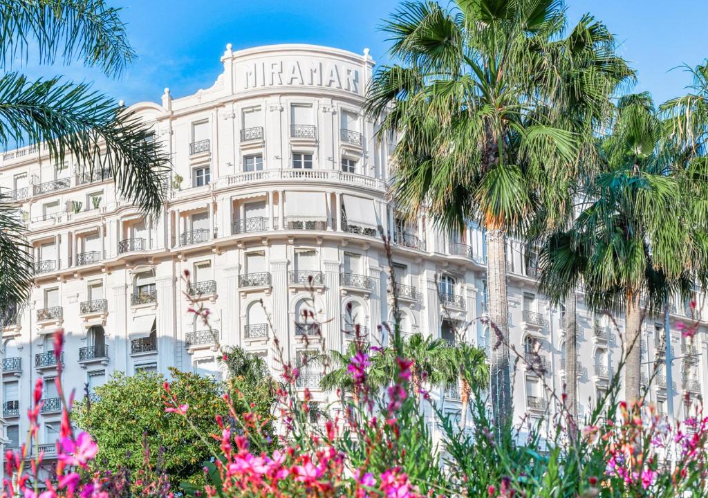 ein hohes weißes Gebäude mit Palmen davor in der Unterkunft Cannes Imperial Croisette Palais Miramar in Cannes
