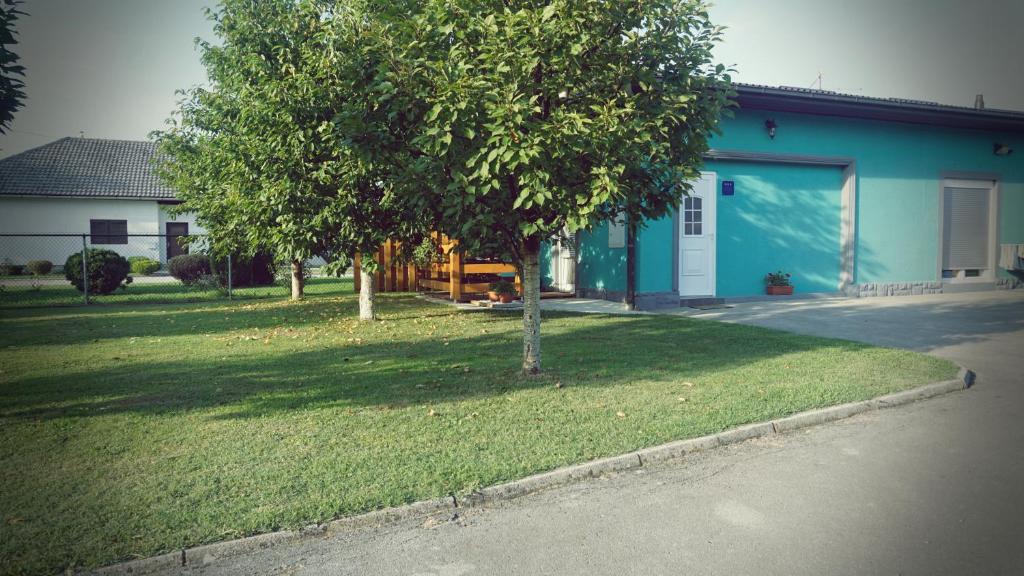 a tree in a yard next to a blue house at Studio apartman Zorkovac in Ozalj