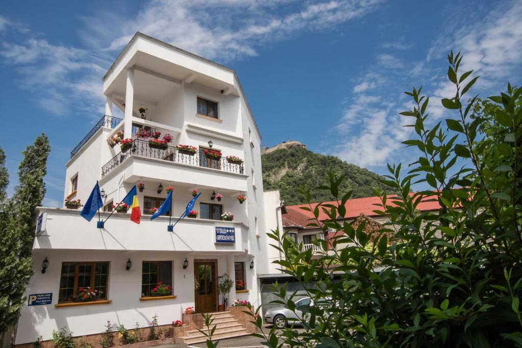 a white building with a balcony and flags on it at Pensiunea Vila Europa in Deva